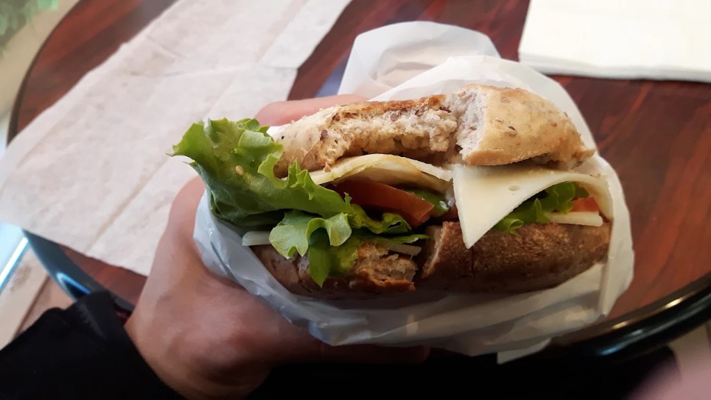 Multigrain bagel sandwich with lettuce, cheese, and tomato, wrapped in paper.