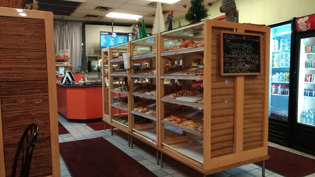 Bakery interior with wood display cases of pastries, orange counter, and drink cooler.