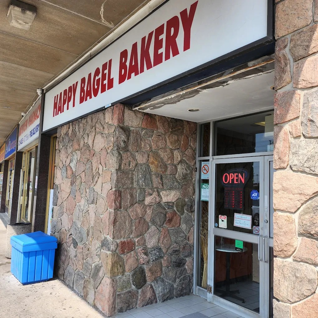 Exterior of Happy Bagel Bakery: red lettering on white sign above a stone facade.